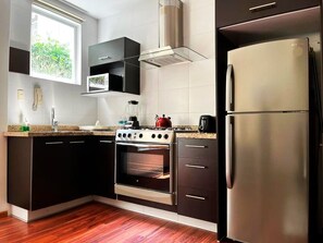 A modern kitchen with a built-in oven, a stainless steel refrigerator, and a window providing natural light.