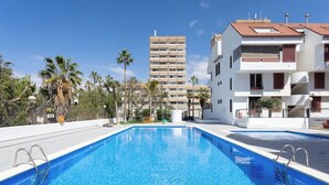 Une piscine à l’eau d’un bleu cristallin, entourée de bâtiments blancs dotés de balcons et de palmiers.