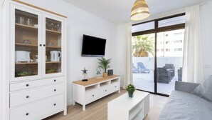 Un salon moderne avec un téléviseur, des meubles blancs, une table basse en bois et une grande fenêtre donnant sur un beau paysage.