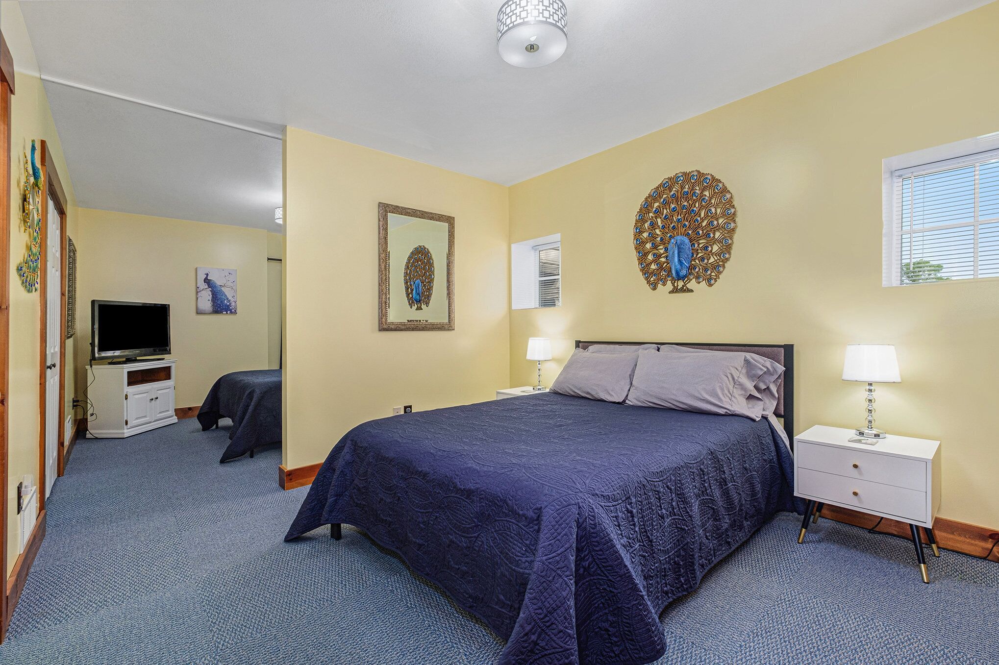 A bedroom with a large bed, a bedside table with a lamp, a television, and artwork on the walls.