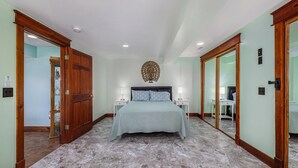 A bedroom with a bed, two bedside tables, a mirror, and a ceiling light fixture. - Renovated Dairy Barn – 4 Bedrooms, 5 Beds, 2.5 Baths, Huge, Accessible & Stylish (Byron Center)
