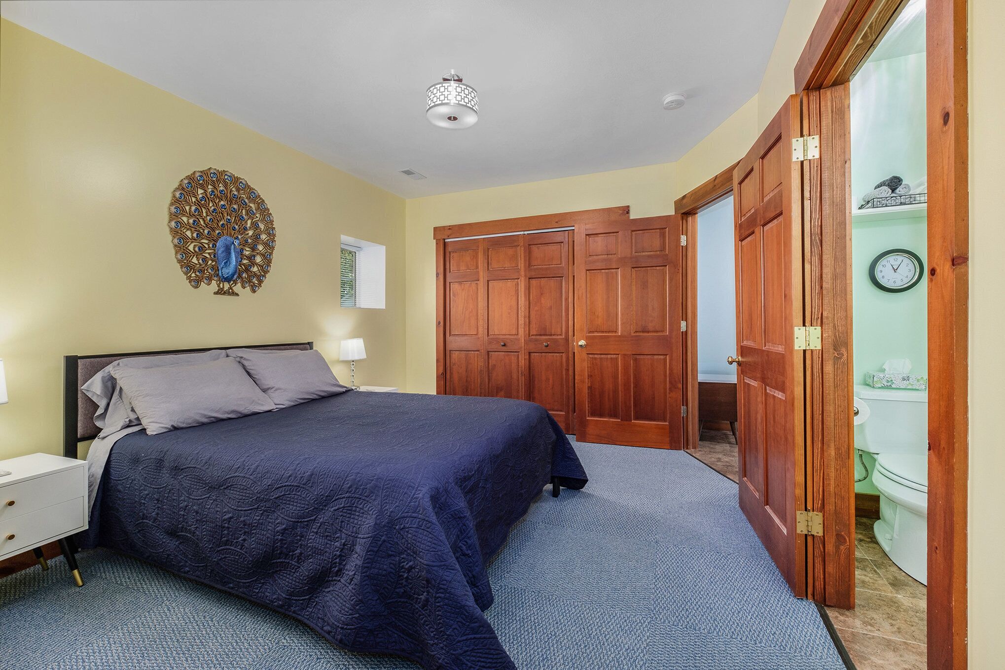 Ein Schlafzimmer mit einem großen Bett, einem Holzschrank und einer Wanddekoration mit Pfau-Motiv.
