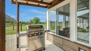 A covered patio with a stainless steel grill, large windows, and a view of a green landscape. - Renovated Dairy Barn – 4 Bedrooms, 5 Beds, 2.5 Baths, Huge, Accessible & Stylish (Byron Center)