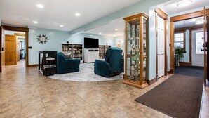 A spacious living room with a large TV, a fireplace, and a bookshelf. - Renovated Dairy Barn – 4 Bedrooms, 5 Beds, 2.5 Baths, Huge, Accessible & Stylish (Byron Center)