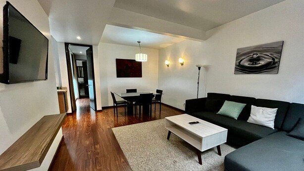 A modern living room with a sofa, coffee table, and a dining area with chairs and a table. - Condesa Residence Amsterdam 203 (Ciudad de México)