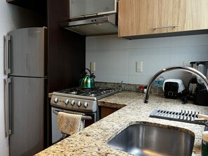 A compact kitchen with a stainless steel refrigerator, a gas stove, a sink, and wooden cabinets.
