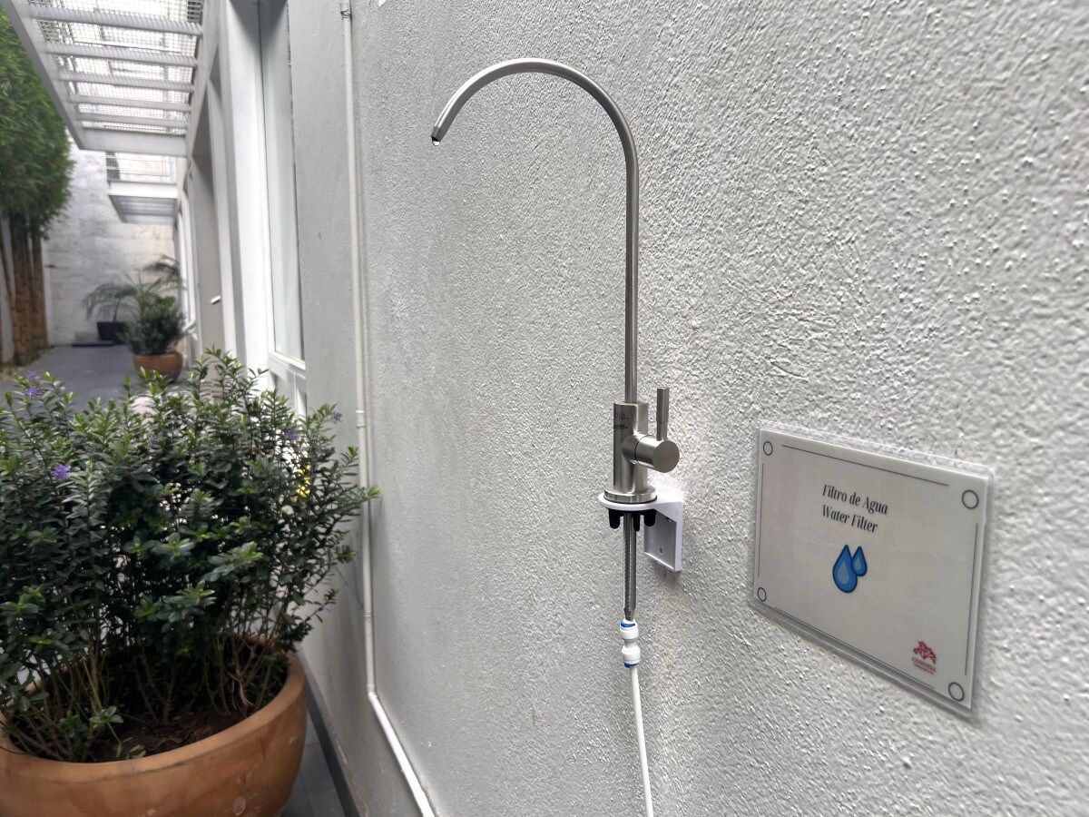 A water filter sign on a wall, a metal showerhead, and a potted plant.