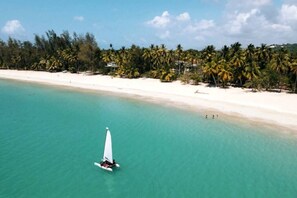 A beach with clear turquoise water, a sailboat, and a line of palm trees in the background.