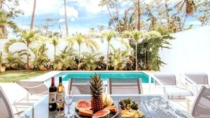 Une table avec un plateau en verre, deux bouteilles de vin, un ananas, des tranches de pastèque et une assiette contenant des légumes et du pain.