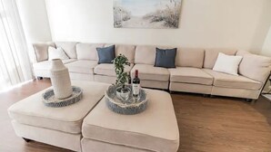 Olohuoneessa on beigenvärinen sohva, koristeellisella alustalla varustettu sohvapöytä ja seinällä taulu.