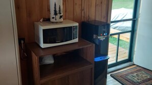 A wooden interior with a microwave on a wooden shelf, a water dispenser, and a sign above stating "HAPPY CAMPERS HAVE 'more fun'".