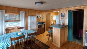 A wooden interior with a dining table, chairs, a kitchen area, and a small bar.