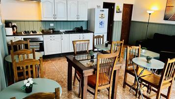 A compact kitchen with white cabinets, a dining area with wooden chairs and a glass table, and a small refrigerator.