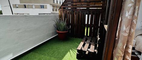 Una terraza en la azotea con césped artificial, una pérgola de madera y una planta en maceta.