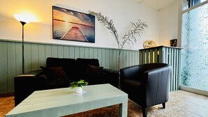 Een zithoek met een bank, fauteuil en salontafel. Er hangt een schilderij aan de muur en staat een plant ernaast.