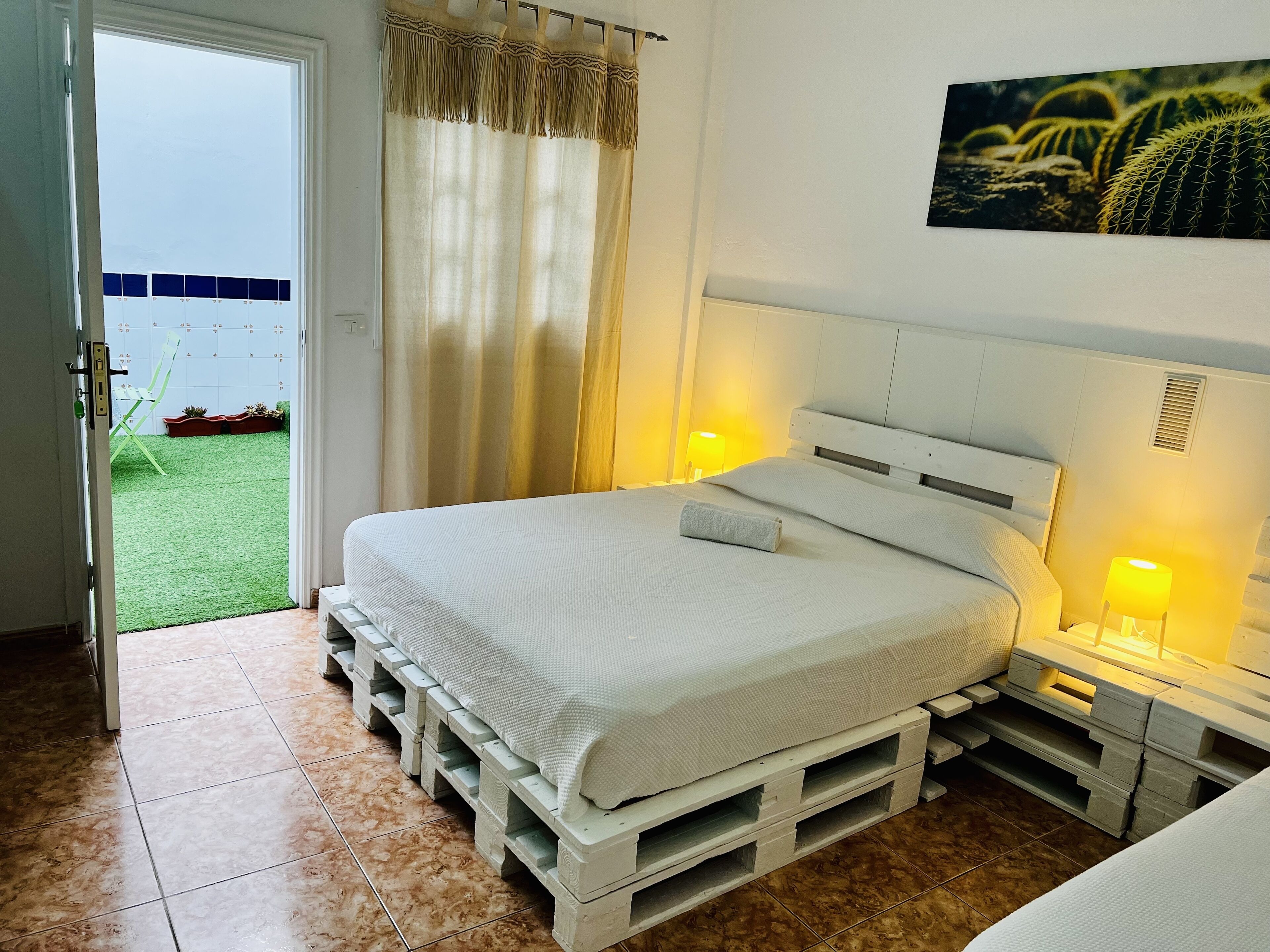 A bedroom with a bed on a pallet, a door to a balcony, and a painting on the wall.