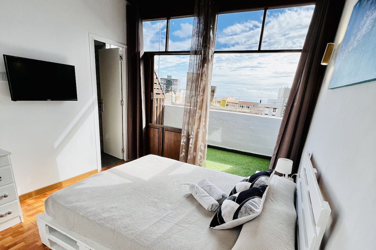 A bedroom with a bed, a TV, a window with a view, and a wooden floor.