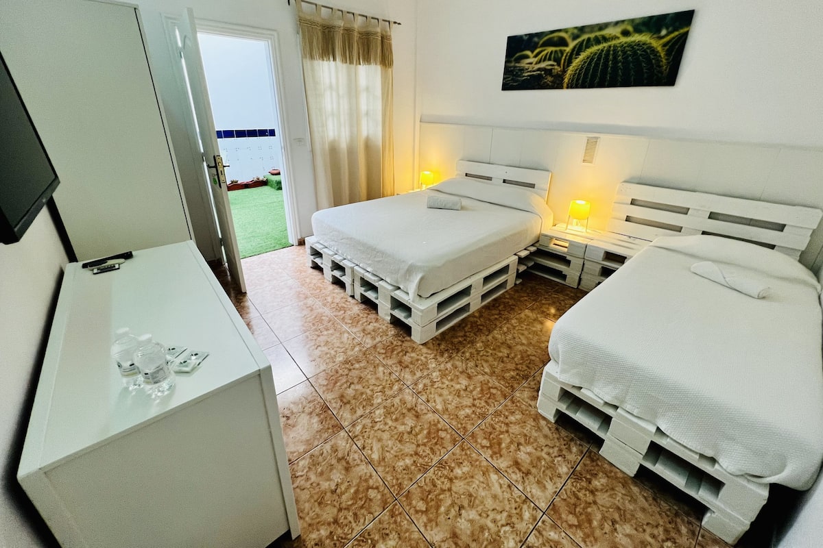 A bedroom with two beds, a desk, and a door leading to a balcony.