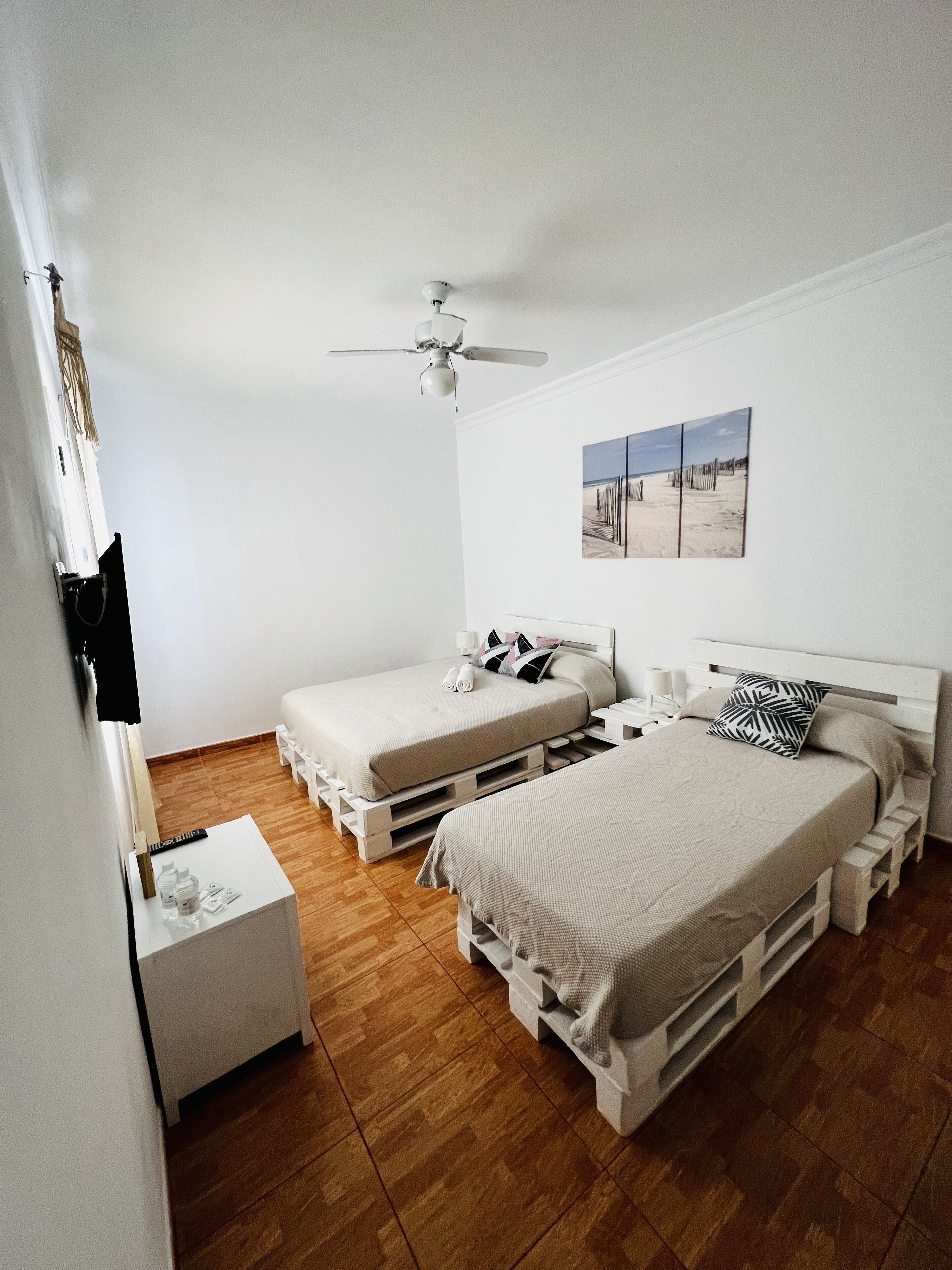 Ein Schlafzimmer mit zwei Betten, einem Deckenventilator, einem Nachttisch und einem Wandbild.