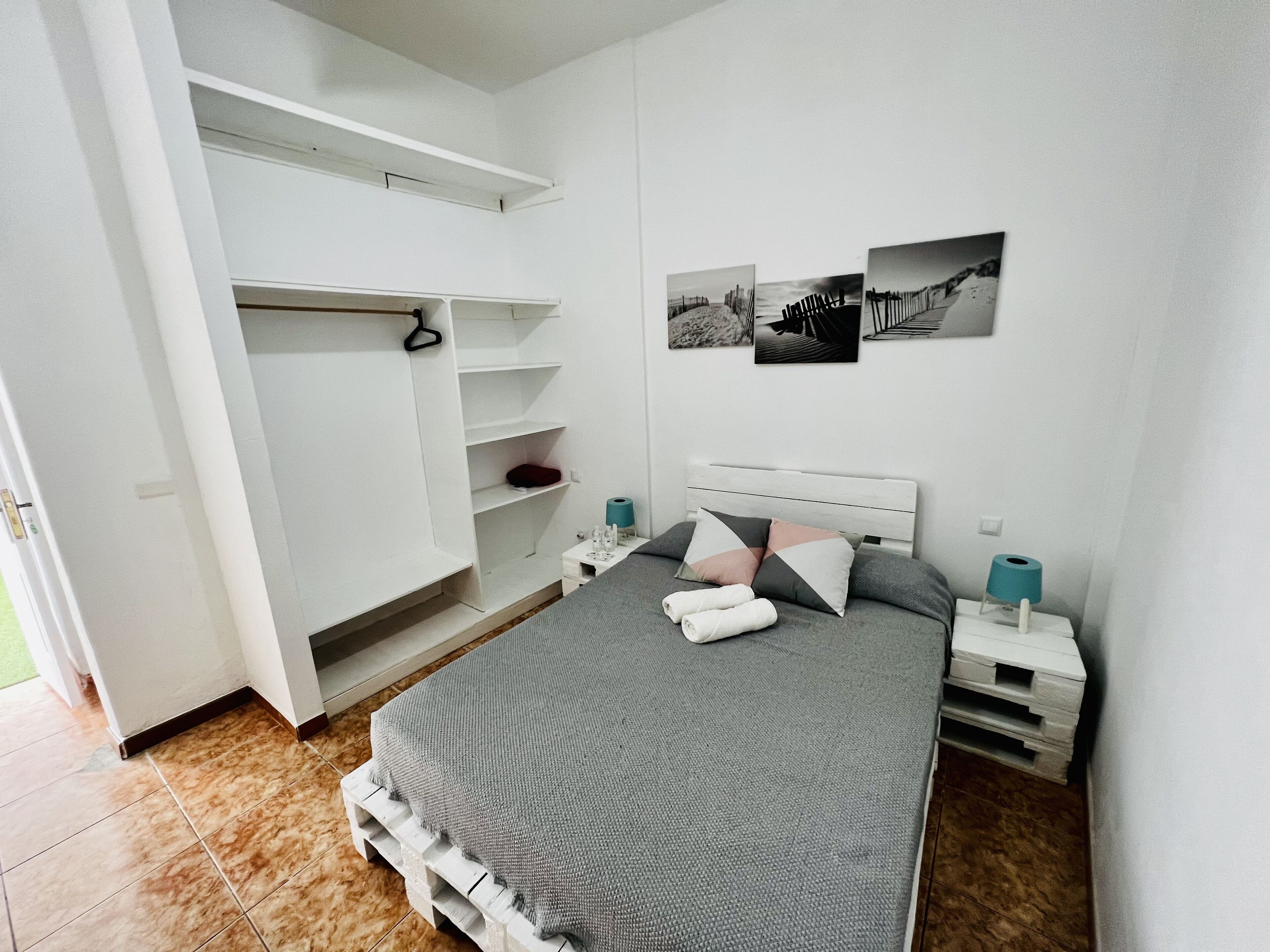 A bedroom with a bed, a wardrobe, a nightstand, and a wall-mounted shelf.
