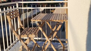 A balcony with a wooden table and chairs, a white railing, and a view of the sea and buildings in the background. - Casa Villaggio Pirandello (Agrigento)