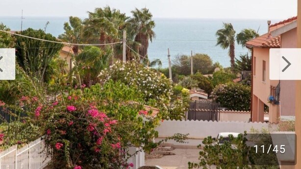 A residential area with a view of the sea, a white fence, and a building with a red roof. - Casa Villaggio Pirandello (Agrigento)