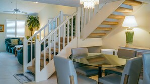 A dining area with a glass table and chairs, a staircase with white railings, and a lamp on a side table. - Beach Access, Pools, Tennis and Pickleball - 1225 Gulf & Bayside (Siesta Key)