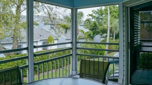 A glass-enclosed balcony with a round table and chairs, overlooking a residential area with houses and greenery. - Beach Access, Pools, Tennis and Pickleball - 1225 Gulf & Bayside (Siesta Key)