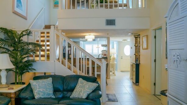 A spacious living area with a green sofa, a potted plant, and a staircase leading to an upper level. - Beach Access, Pools, Tennis and Pickleball - 1225 Gulf & Bayside (Siesta Key)