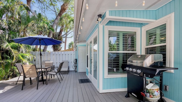 A covered outdoor deck with a grill cart, outdoor seating, and a blue umbrella. - 15 SS Cottage - Close to Beach and Village (Siesta Key)
