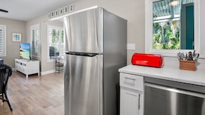 A modern kitchen with a stainless steel refrigerator, a white countertop, and a window with a view of greenery. - 15 SS Cottage - Close to Beach and Village (Siesta Key)