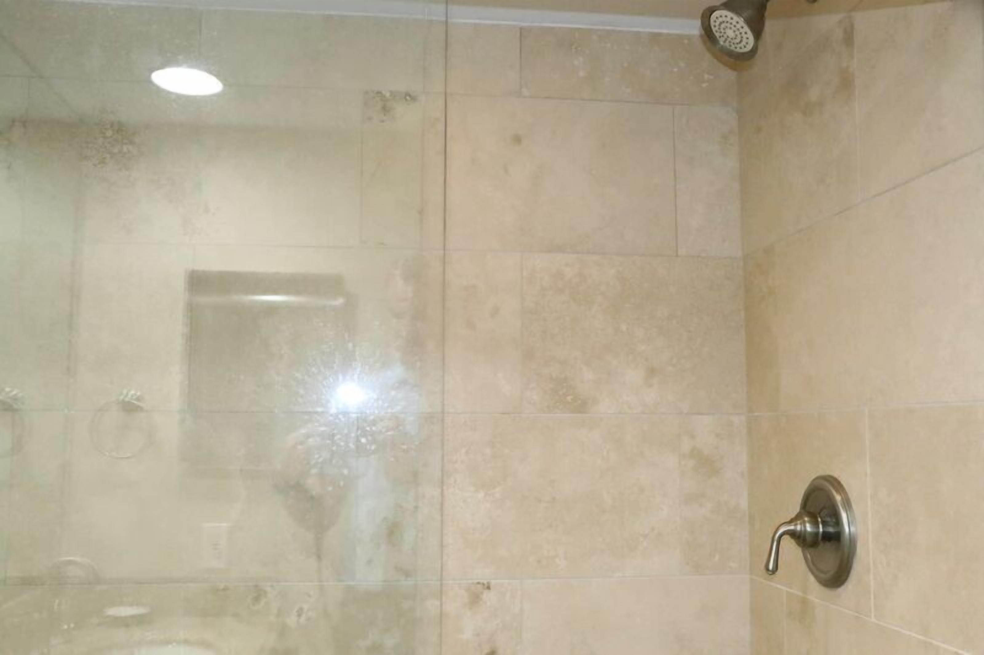 A bathroom with beige tiles, a showerhead, and a visible door handle.
