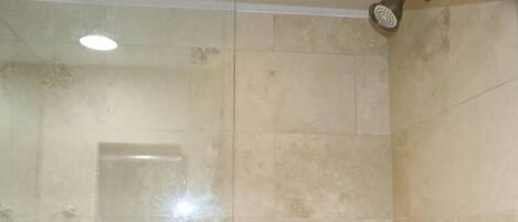 A bathroom with beige tiles, a showerhead, and a visible door handle.