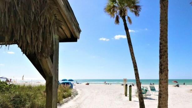 A beach with a thatched structure, palm trees, and beach chairs. - 303 Sea Shell- Beautifully Updated Gulfside Condo (Siesta Key)