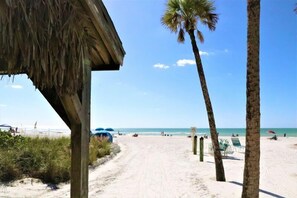 A beach with a thatched structure, palm trees, and beach chairs. - 303 Sea Shell- Beautifully Updated Gulfside Condo (Siesta Key)