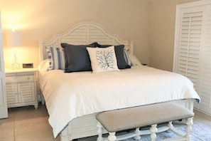 A neatly made bed with a white headboard, a bedside table with a lamp, and a bench at the foot of the bed.