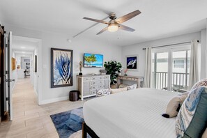 A bedroom with a bed, a ceiling fan, a desk, and a view through a sliding door.