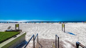 A beach with a clear sky, a sandy area with a few people, and a paved walkway leading to the beach. - 704S Crescent Arms – Full Gulf Front View (Siesta Key)