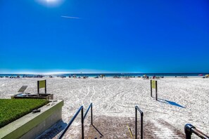 Ein Strand mit blauem Himmel, einem sandigen Bereich mit einigen Personen und einem gepflasterten Weg zum Strand.