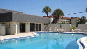 A swimming pool with lounge chairs, a building with a tiled roof, and palm trees in the background. - 704S Crescent Arms – Full Gulf Front View (Siesta Key)