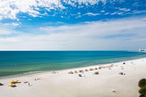 A beach with clear blue water, sandy shore, and umbrellas.