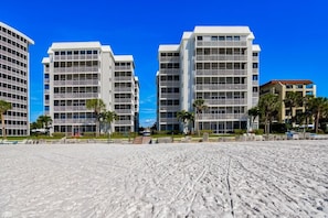 Ein Hotel direkt am Strand mit mehrstöckigen Gebäuden, einem Sandstrand im Vordergrund und Palmen.