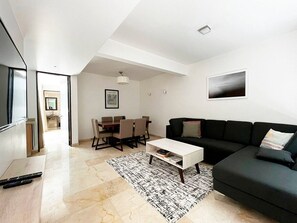 A modern living room with a black sofa, a white coffee table, and a dining area with a table and chairs.