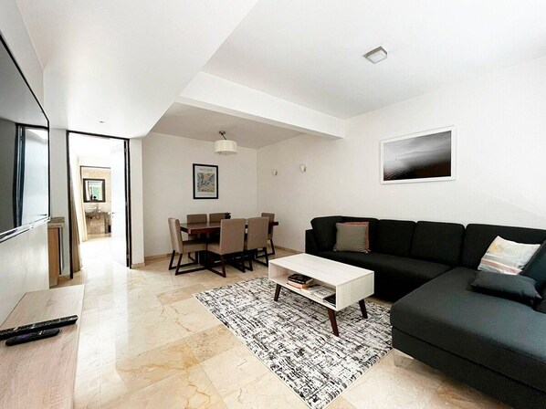 A modern living room with a black sofa, a white coffee table, and a dining area with a table and chairs.
