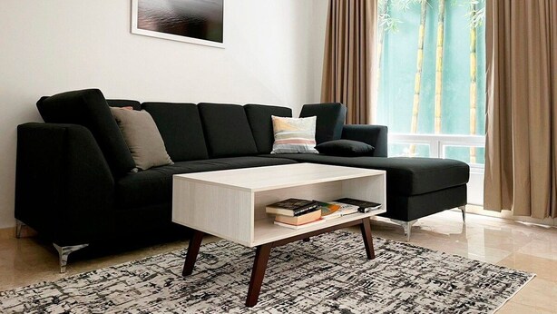 Una sala de estar moderna con un sofá seccional negro, una mesa de centro blanca y una alfombra estampada.