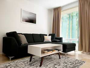 A modern living room with a black sectional sofa, a white coffee table, and a patterned rug.