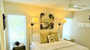 A hotel room with a bed, two bedside lamps, a ceiling fan, and a painting on the wall. - Ground-level Condo near Beach and Shops - Casa Siesta 2 (Siesta Key)