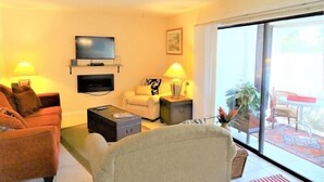 A living room with a sofa, armchair, TV, and a balcony with a table and chairs. - Ground-level Condo near Beach and Shops - Casa Siesta 2 (Siesta Key)