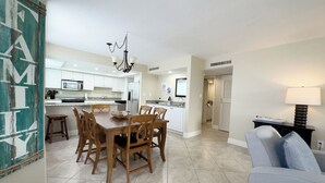 Een moderne keuken met witte kasten, een eethoek met houten stoelen en een woonkamer met een blauwe bank.
