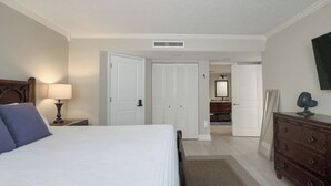 Een slaapkamer met een bed, een dressoir, een nachtkastje, een lamp en een spiegel.